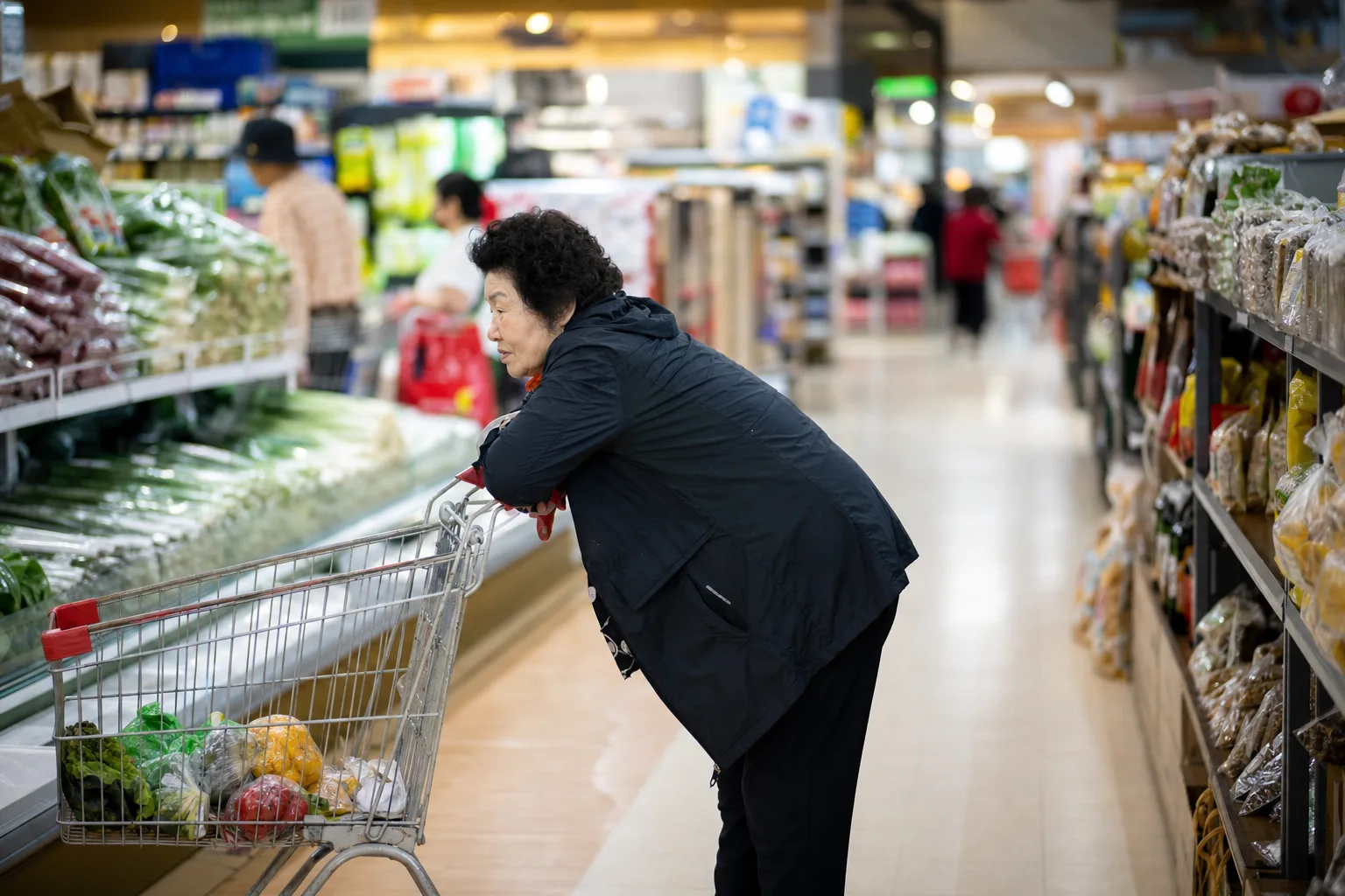 마트에서 쇼핑카트 손잡이에 상체를 기대어 허리를 숙인 채 걷는 노년 여성 — 허리를 굽히면 편해지는 척추관협착증의 특징, 향동 경희미르애한의원 통증 칼럼